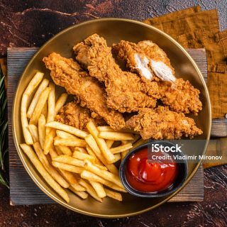Fried Breaded chicken tender strips with french fries and tomato ketchup on a plate. Dark backgrund. Top view.